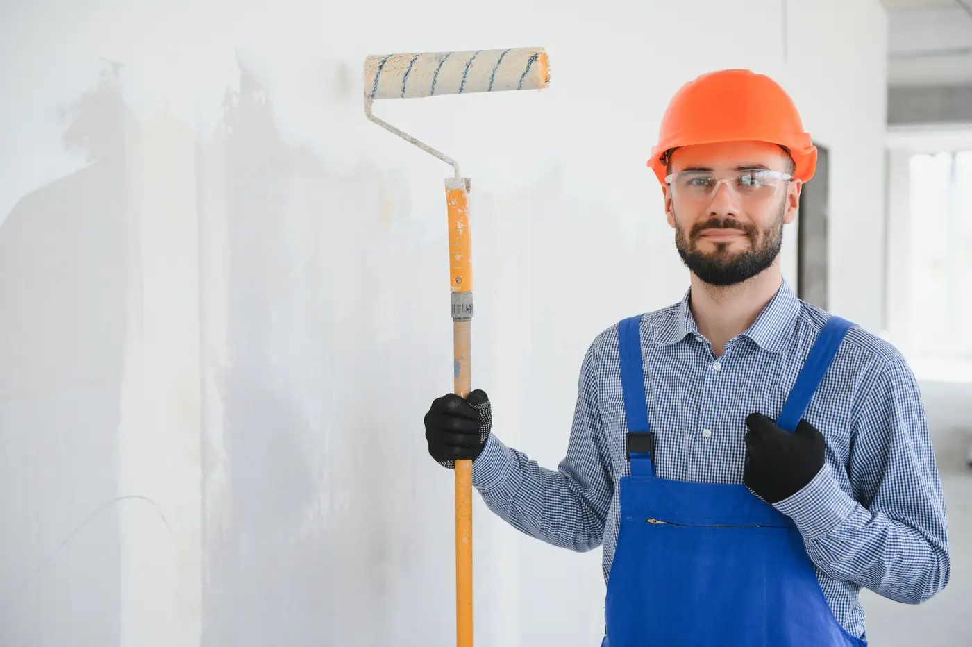 Professional painter with blue coveralls and hard hat, holding paint roller