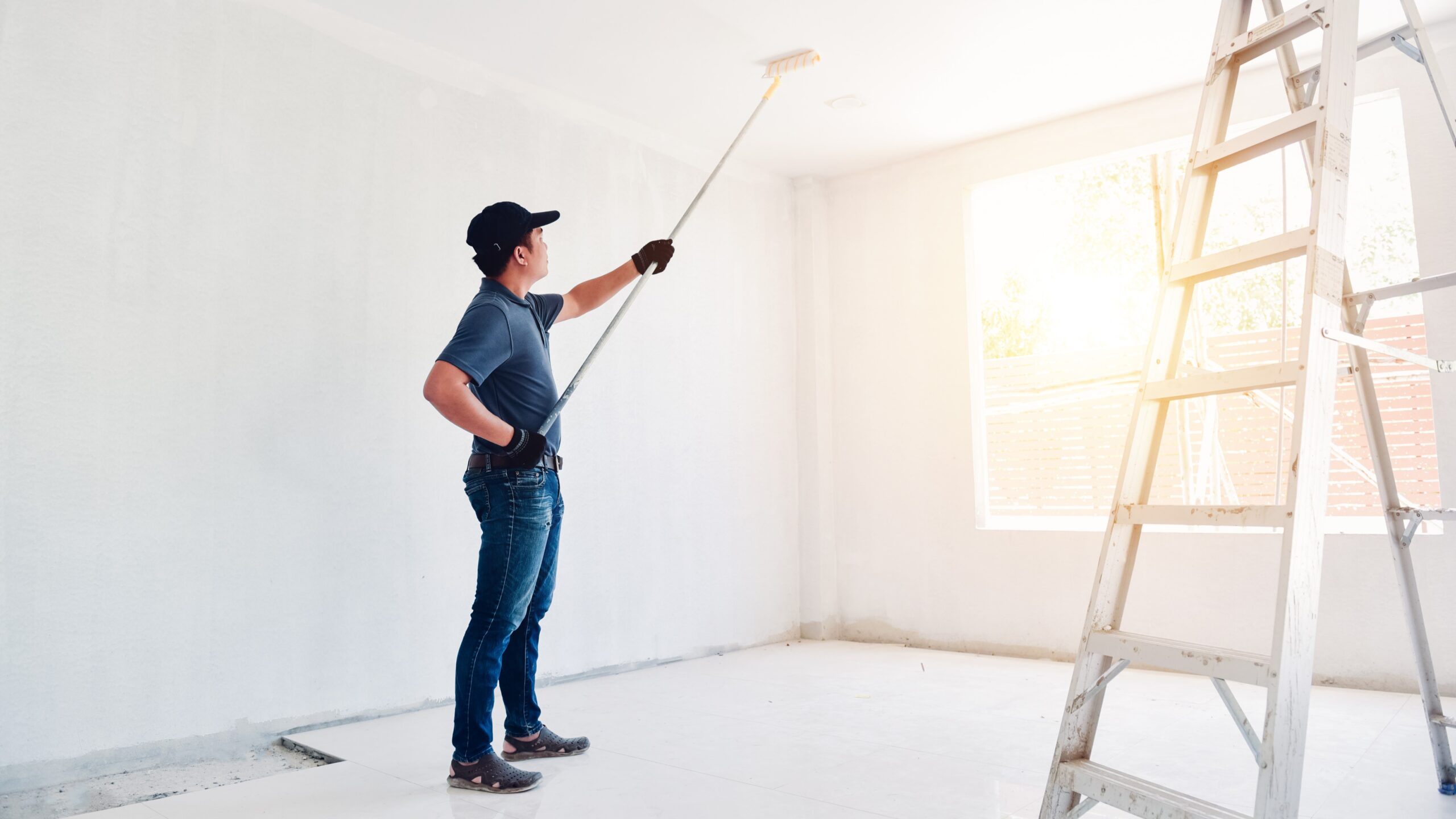 Man painting bedroom ceiling with white paint